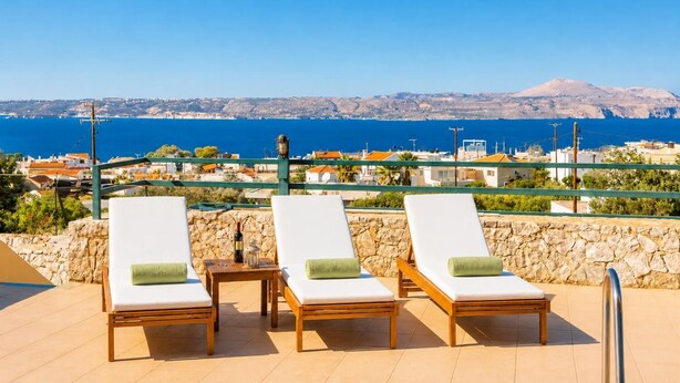 Una terraza con tres sillones, una mesa y vistas al mar y montañas distantes.