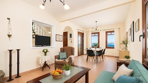 Amplia sala de estar con sofá, mesa de centro, televisor, mesa de comedor y vista al mar.