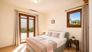 Un dormitorio con cama, una mesita de noche pequeña con lámpara, una ventana con cortinas y un aire acondicionado.