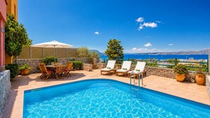 Zona de piscina con sillones de descanso, una mesa y vista al mar.