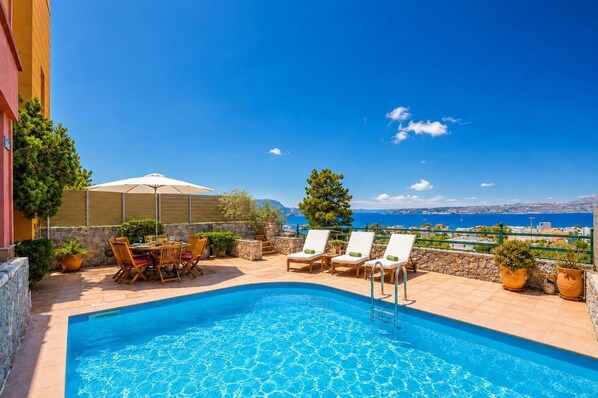 Un espace piscine avec des chaises longues, une table et une vue sur la mer.