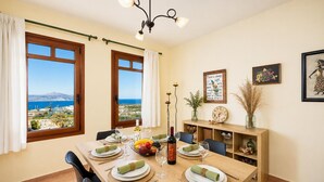 Comedor con una mesa dispuesta para cuatro personas, ventanas amplias con cortinas, una araña y decoración en las paredes.