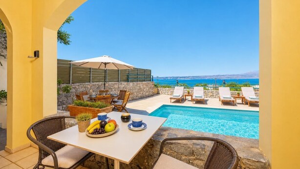 Un espace aménagé au bord de la piscine, avec une table pour deux, un panier de fruits et des chaises longues près de la piscine.