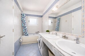 Ein Badezimmer mit einer Badewanne, zwei Waschbecken, einer Waschmaschine und einem großen Spiegel.
