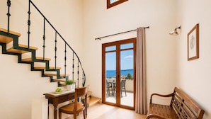 Un escalier avec des marches en bois et des rampes noires, un bureau avec une chaise, un banc en bois et une porte-fenêtre coulissante donnant sur un espace extérieur avec vue sur la mer.