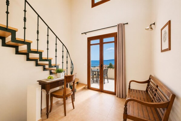 A staircase with wooden steps and black railings, a desk with a chair, a wooden bench, and a sliding glass door leading to an outdoor area with a view of the sea. - Villa Aphrodite - Four Bedroom Villa, Sleeps 7 (Plaka)