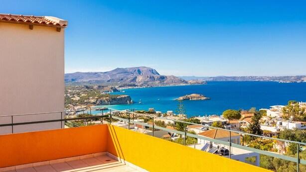A balcony with a clear view of a coastal town, a mountain, and the sea.