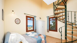 A bedroom with a bed, a wardrobe, a window with a view, a lamp, and a spiral staircase.
