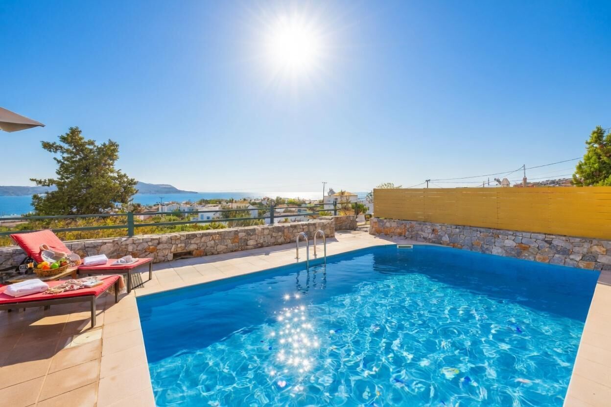 Une piscine dotée de chaises longues et bordée d’un mur en pierre, offrant une vue sur un paysage côtier.
