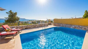A swimming pool with lounge chairs and a stone wall, overlooking a coastal landscape.