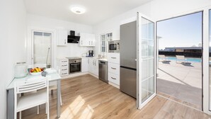 A modern kitchen with white cabinetry, a stainless steel refrigerator, and a dining area with a glass table. - Villa Yaiza Secret 3 (Yaiza)