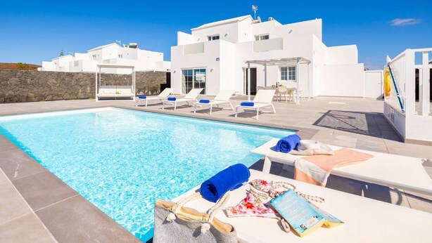 A modern white building with a swimming pool, lounge chairs, and a stone wall. - Villa Yaiza Secret 3 (Yaiza)