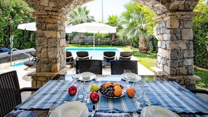 An outdoor dining area with stone pillars, a pool, and chairs. - Villa Tara - Three Bedroom Villa, Sleeps 6 (Oludeniz)