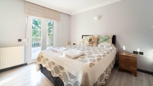 A bedroom with a large bed, a nightstand, a wall-mounted light, and a sliding glass door to a balcony. - Villa Tara - Three Bedroom Villa, Sleeps 6 (Oludeniz)