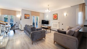 A spacious living room with a sofa set, a TV, and a fireplace. - Villa Tara - Three Bedroom Villa, Sleeps 6 (Oludeniz)
