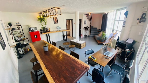 A spacious living area with a large wooden dining table, a kitchen area with a red appliance, and a staircase leading to another level. - Music Guest House (Mexico City)