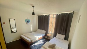 A hotel room with two single beds, a small round table, a mirror, and a window with curtains. - Music Guest House (Mexico City)
