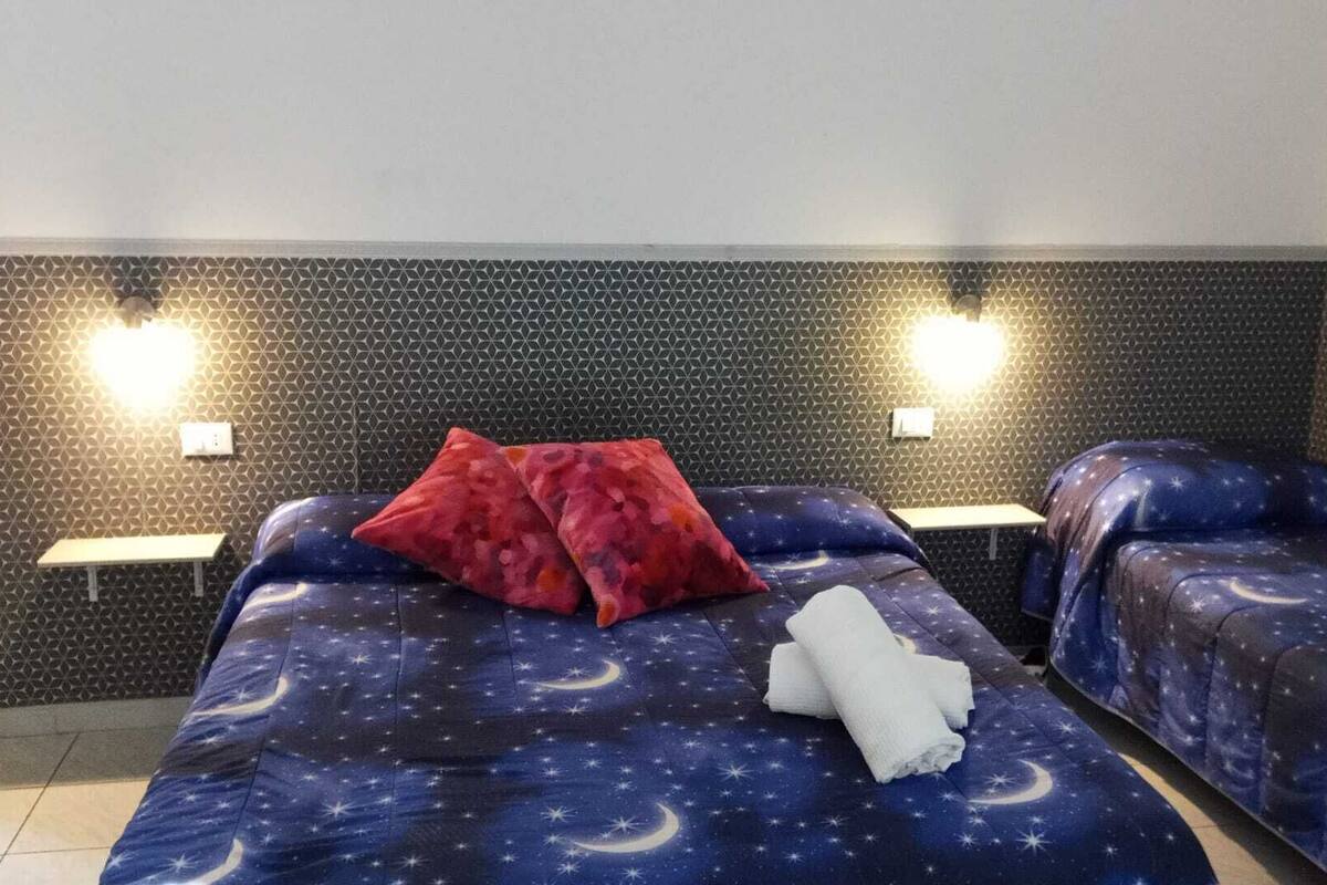 A hotel room with two beds, each with a starry night theme. There are two wall-mounted lights on either side of the beds.