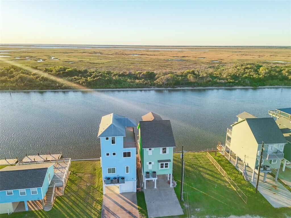 Un quartier résidentiel avec des maisons situées près d’un plan d’eau, comprenant une grande maison avec un garage et une plus petite maison avec un porche.