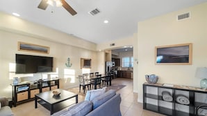 A spacious living room with a large sofa, a TV, and a dining area with chairs and a table.
