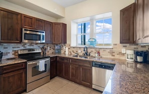 A kitchen with wooden cabinets, stainless steel appliances, a granite countertop, and a window with a view.