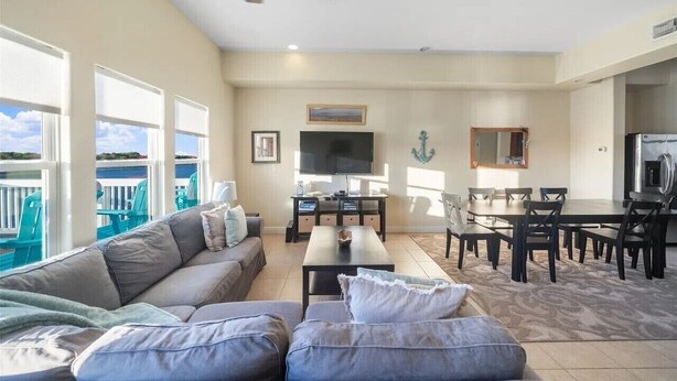 A spacious living room with a large TV, comfortable seating, a dining area, and a view of the ocean.