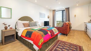 A modern bedroom with a large bed, a side table, a television, and a view of the outdoors through a window. - The Eades Store Projects Studio (London)