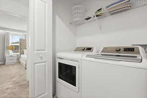 Un cuarto de lavandería con dos lavadoras blancas y un tendedero encima.