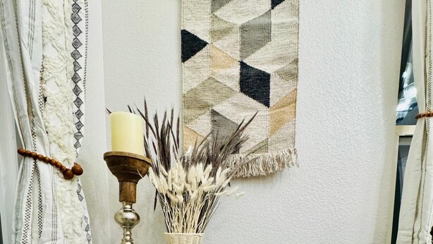 A corner room with a round blue mosaic table, a candle, and a vase with dried plants. A geometric patterned tapestry hangs on the wall. - 5BR Greeley Home - Sleeps 14, Pets Ok, EV Charger (Greeley)