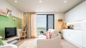 Een moderne woonkamer met een bank, televisie en uitzicht op de stad door een groot raam.