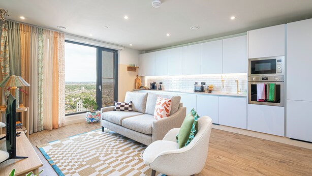 Een moderne woonkamer met een bank, fauteuil en stadszicht door grote ramen.