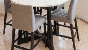 A round dining table with four grey upholstered chairs, a white marble top, and a candle centerpiece. - Minutes to EVERYTHING! Gated home! AC in all rooms! (Hatillo)