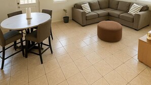 A living room with a round dining table, a brown sectional sofa, a small round ottoman, and a chandelier. - Minutes to EVERYTHING! Gated home! AC in all rooms! (Hatillo)