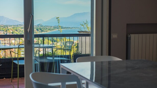 A balcony with a view of a lake and mountains, furnished with tables and chairs. - La Casa sulla Collina (Padenghe sul Garda)