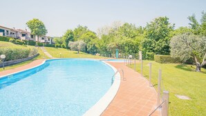 A swimming pool with a tiled deck, surrounded by well-maintained grass and trees. - La Casa sulla Collina (Padenghe sul Garda)