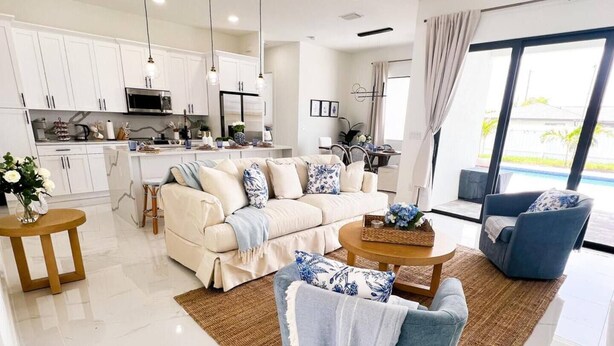 A spacious living room with a sofa, armchairs, and a coffee table. A kitchen with white cabinets and a dining area with a table and chairs are visible. - Beautiful Cape Coral Getaway with Sparkling Pool & Relaxing Outdoor Space! (Cape Coral)