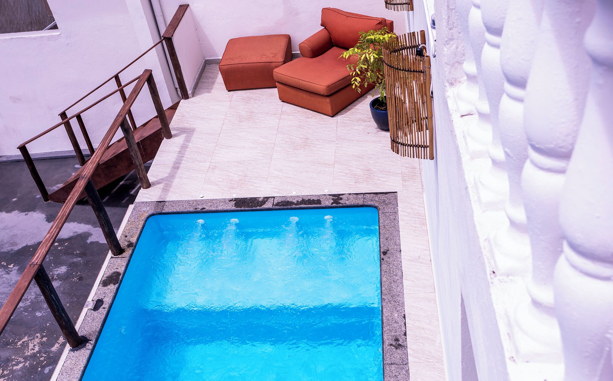 A pool area with a blue pool, wooden deck, and a seating area with cushions.
