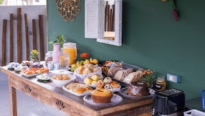 A breakfast buffet with various food items and a toaster on a wooden table against a green wall. - Pousada Cahê (Ilhabela)
