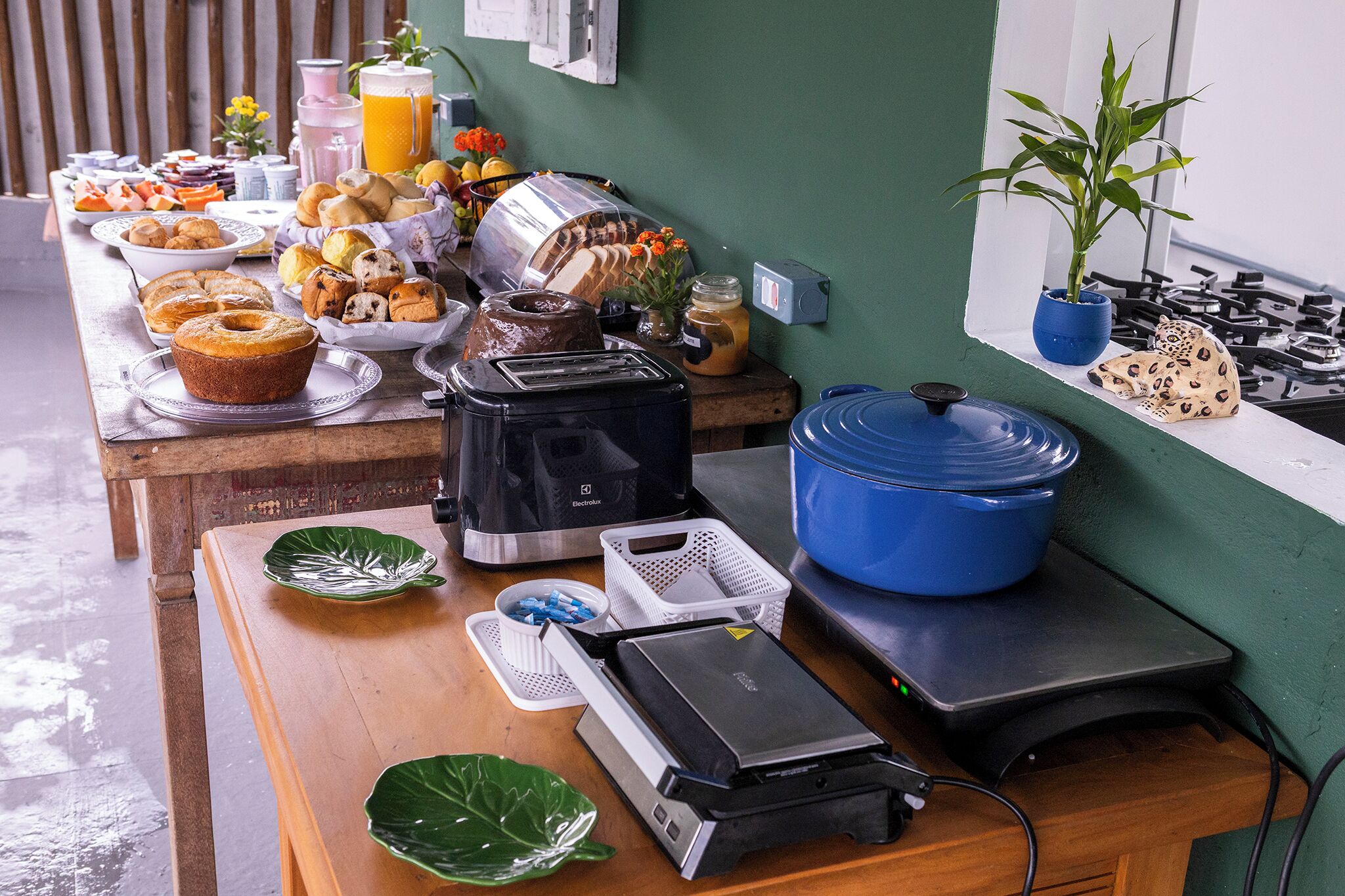 A breakfast buffet with various pastries, a coffee machine, and a blue slow cooker on a wooden table.