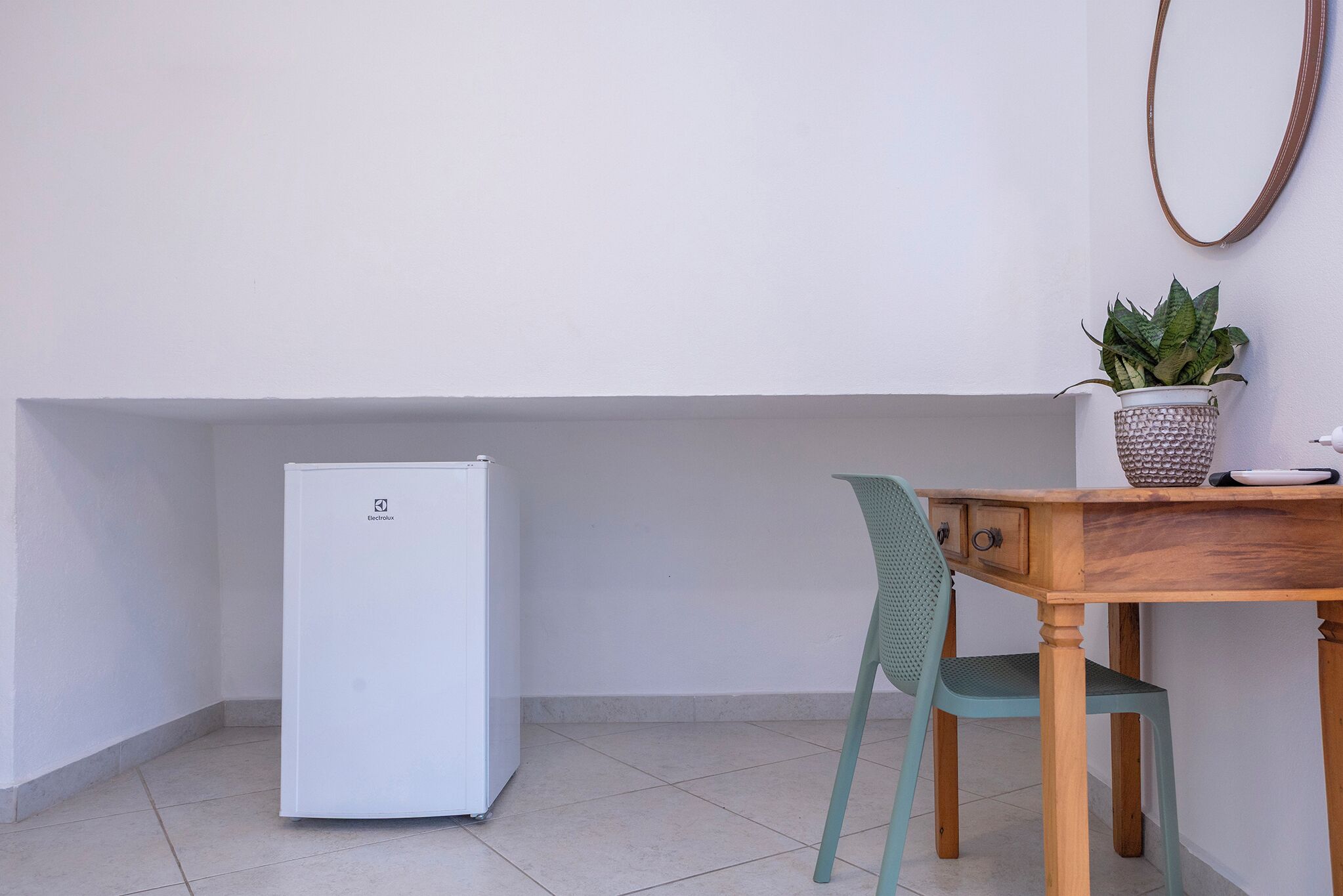 A compact kitchen with a white refrigerator, a wooden table, a green chair, and a potted plant.