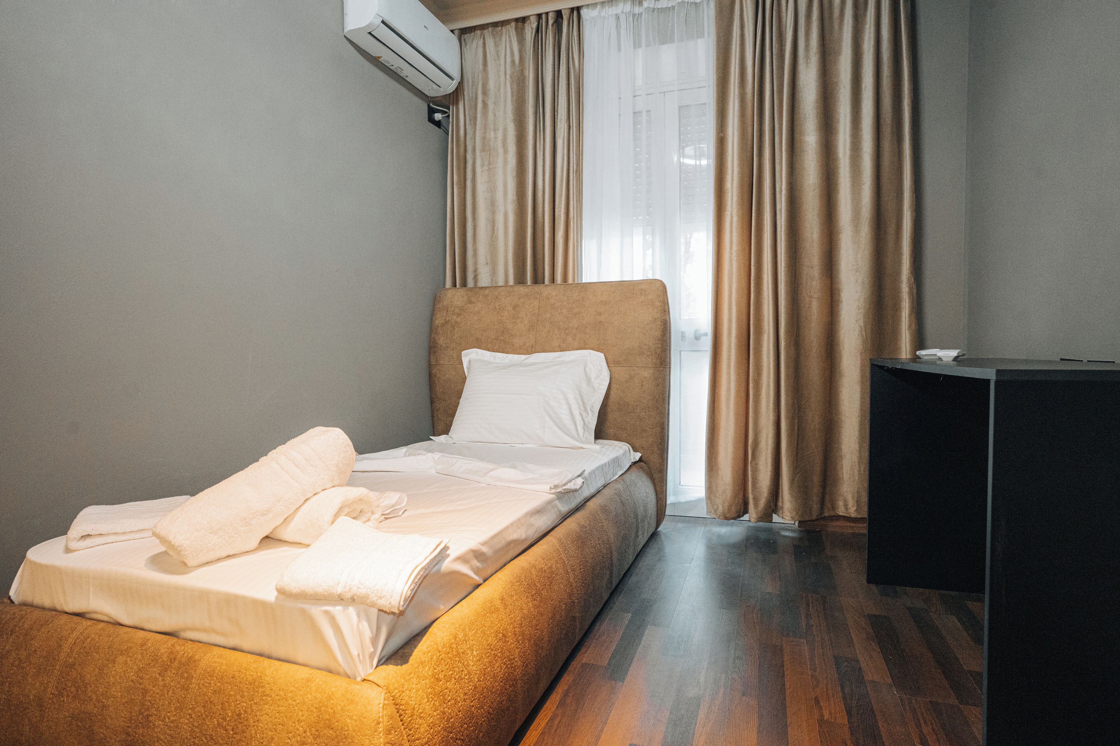 A neatly made bed with white linens and towels, a brown headboard, and a wooden floor.