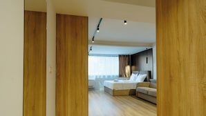 Una camera d'albergo moderna con pavimento in legno, un letto, una poltrona e un'ampia finestra con tende.