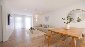 A modern living room with a wooden dining table, a sofa, and a large mirror.