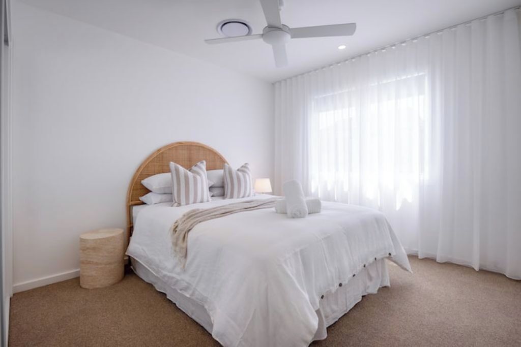 Une chambre à coucher avec un lit, un ventilateur de plafond et une fenêtre ornée de rideaux légers.