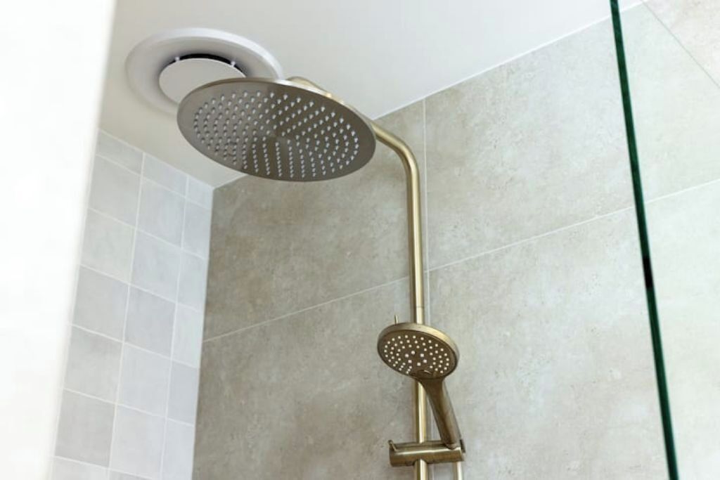 Chuveiro com chuveiro dourado e painel de controle fixado na parede.