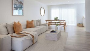 A modern living room with a white sofa, a coffee table, and a dining table with chairs. - Olas Villa 2 | Luxe 3BR · Plunge Pool · Near Beach (Anna Bay)