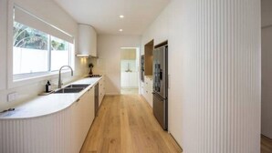 A modern kitchen with a central island, stainless steel appliances, and a window providing natural light. - Olas Villa 4 | Luxe 3BR · Plunge Pool · Near Beach (Anna Bay)