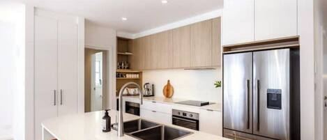 A modern kitchen with white cabinets, a stainless steel refrigerator, and a central island with a sink.