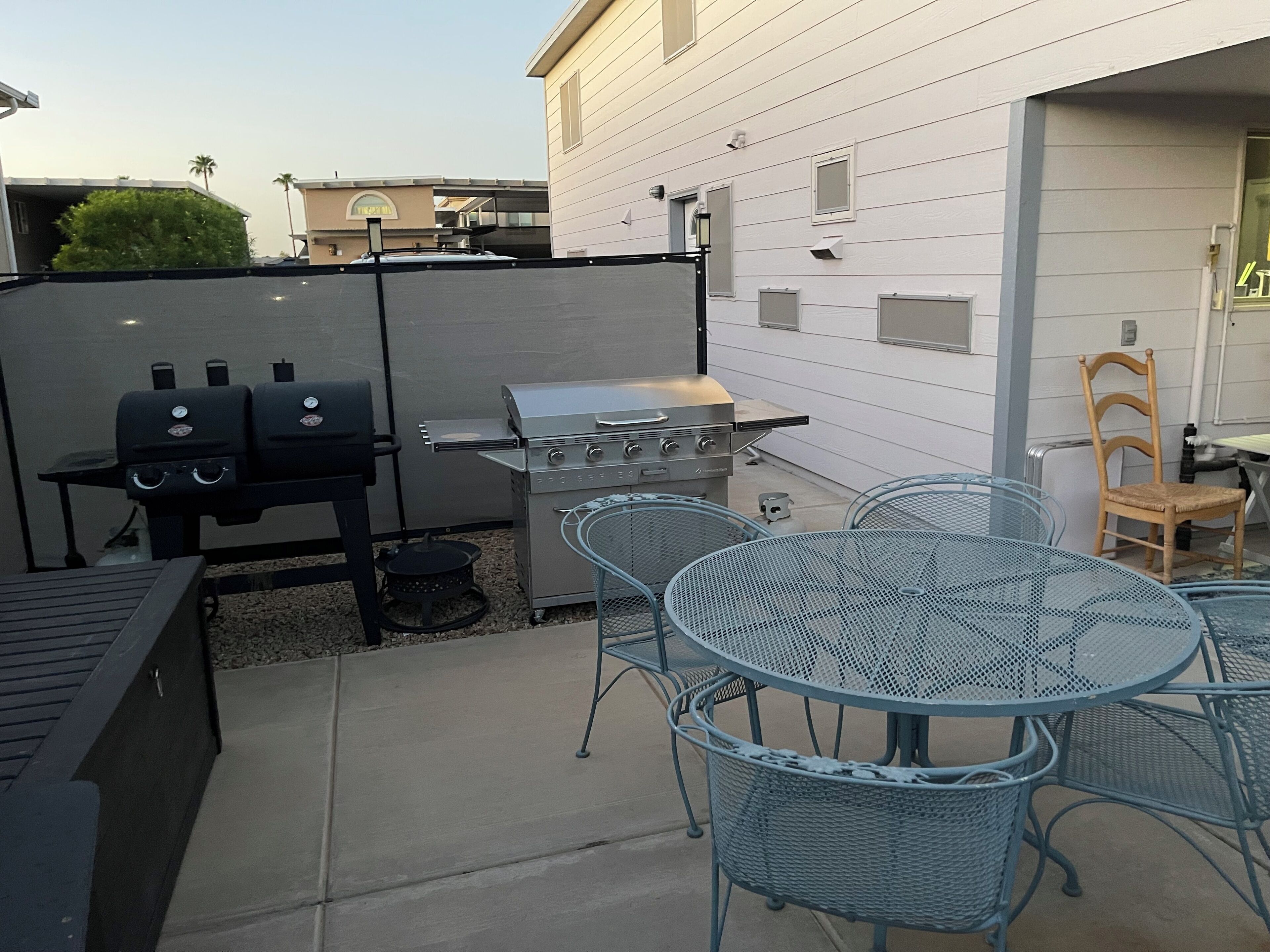 An outdoor patio with a grill, metal chairs, and a table.