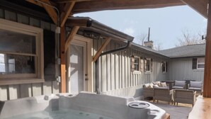 Un jacuzzi bajo una pérgola de madera con vista a una casa al fondo.